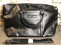 Front view of Michel Germain black faux leather duffle bag with handles and shoulder strap