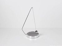 Full view of silver magnetic decision maker showing swing arm, ball and circular base