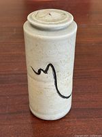 Front view showing cylindrical jar with lid and black abstract brushstroke