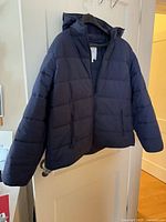 Front view of navy Hudson North hooded puffer jacket hanging on door