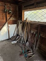 Group of long-handle shovels, rakes, post-hole digger and cutting tools in shed corner