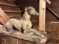 Front angled view of recumbent greyhound statue on base