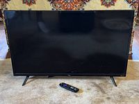 Front view of TCL 32" Roku TV on stand with remote placed below