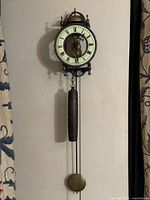 Full view of wall-mounted skeleton clock with weight and pendulum