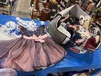 Two dresses and basket with assorted baby girl clothes on table
