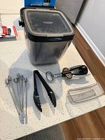 All items laid out: OXO container, skewers, tongs, corkscrew, clear lid