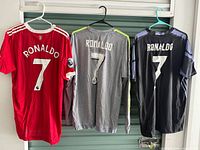 All three Ronaldo jerseys hanging: red Manchester United, grey Real Madrid, black Real Madrid