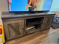 Front view of dark wood entertainment center with TV on top, showing two barn-style cabinet doors and open center shelves