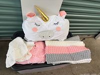 Unicorn sleeping bag atop storage bin with three knitted pieces visible