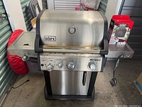 Front view of Weber Spirit stainless steel gas grill showing lid, control panel, side shelves and cabinet