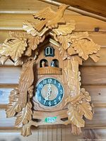 Front view of carved wood cuckoo clock with birds, dial, weights, pendulum