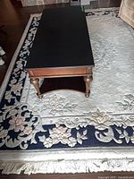 Full view showing rug under coffee table, ivory field, navy border, floral pattern, fringe visible