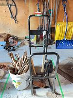 Full view of hand truck, axe, hammers, bucket of kindling