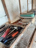 Shelf with black plastic toolbox containing hand tools and green case behind