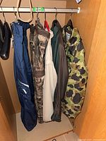 Five garments hanging: blue pants, camo jacket, white jacket, green jacket, camo jacket