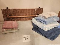 Stack of seven assorted towels and wicker wall-mounted rack with wood bar