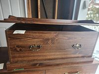 Exterior of wooden chest with lid partially open showing brass-tone handles and raised base