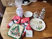 all items laid out on table including oven mitts, pot holder, mug, plates, glass tree jar, snowman ornament