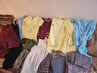 Overview of assorted dresses, jackets, tops and pants on sofa
