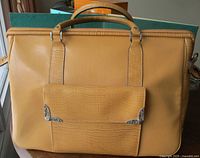 Front view of butterscotch faux leather travel bag showing handles, pocket and hardware