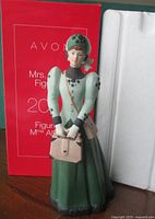 Full view of figurine in front of red Avon box and foam insert