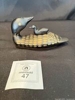 Left profile of brass loon bank with baby and lot tag