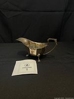 Left side view of tarnished sterling silver gravy boat showing paneled body, handle, and three of four legs
