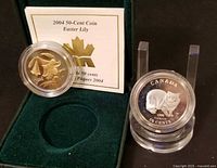 Both coins, Easter Lily coin in open RCM velvet box with insert, Cymric Cat coin standing in capsule