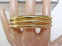 Three matching gold bangles stacked on mannequin hand