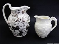 Front view of both Wedgwood pitchers showing embossed designs and relative sizes