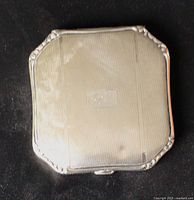 Closed compact front showing engine-turned pattern and monogram