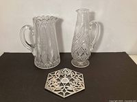Both crystal pitchers and silver trivet displayed