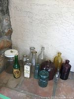 Vintage glass jars and bottles of various sizes and colors arranged on a tiled floor against a wall