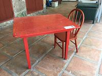 Side view of red wooden kid-sized table and matching chair on tile floor.