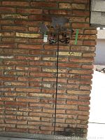 Full view of metal cat weather vane mounted against brick wall showing the entire weather vane including cat figure, directional markers, and mounting rod.