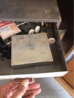 Open drawer showing vintage Super-Calfeg Service Parts box and other small hardware items inside a metal cabinet drawer.