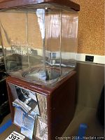 Front and side view of the vintage gumball machine showing brown metal base and clear glass container with embossed branding.