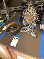 Photo showing antique flat iron with wooden handle next to ornate cherub decorated clock.