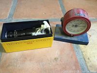 Bell and Howell 16mm anamorphic projection lens in yellow box and red vintage Kodak timer on blue wooden mount.