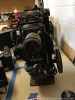 Side view of vintage optical projector with visible lens and adjustment knobs.