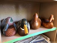Four vintage wooden ducks displayed on a shelf, two painted and two natural wood.