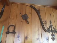 Photo showing a metal horse collar shackle, rusted metal curry comb, and a black metal filigree cross mounted on a wood-paneled wall.