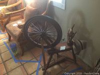 Photo showing full spinning wheel with 22-inch dark spoked wheel, wooden frame, and legs.