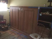 Closed oak Murphy bed cabinet mounted on wall, two large panel doors visible