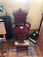 Full view of antique wood chair with red velvet upholstery and small wooden step stool in front.