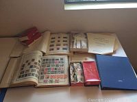 Photo of multiple stamp albums and boxes containing loose stamps arranged on a flat surface.