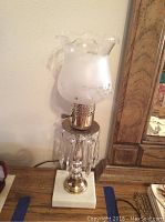 Pair of brass table lamps shown each with scalloped frosted glass shades, hanging crystal-like pendants, and stone-textured bases