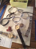 Photo showing assortment of watches with metal and leather straps along with cufflinks on a table.
