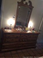 Full view of the wood dresser showing top surface, drawers, and attached mirror frame with items on dresser surface.