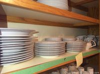 Shelves filled with stacks of white Kent China dinnerware including plates and cups in the Flair pattern.